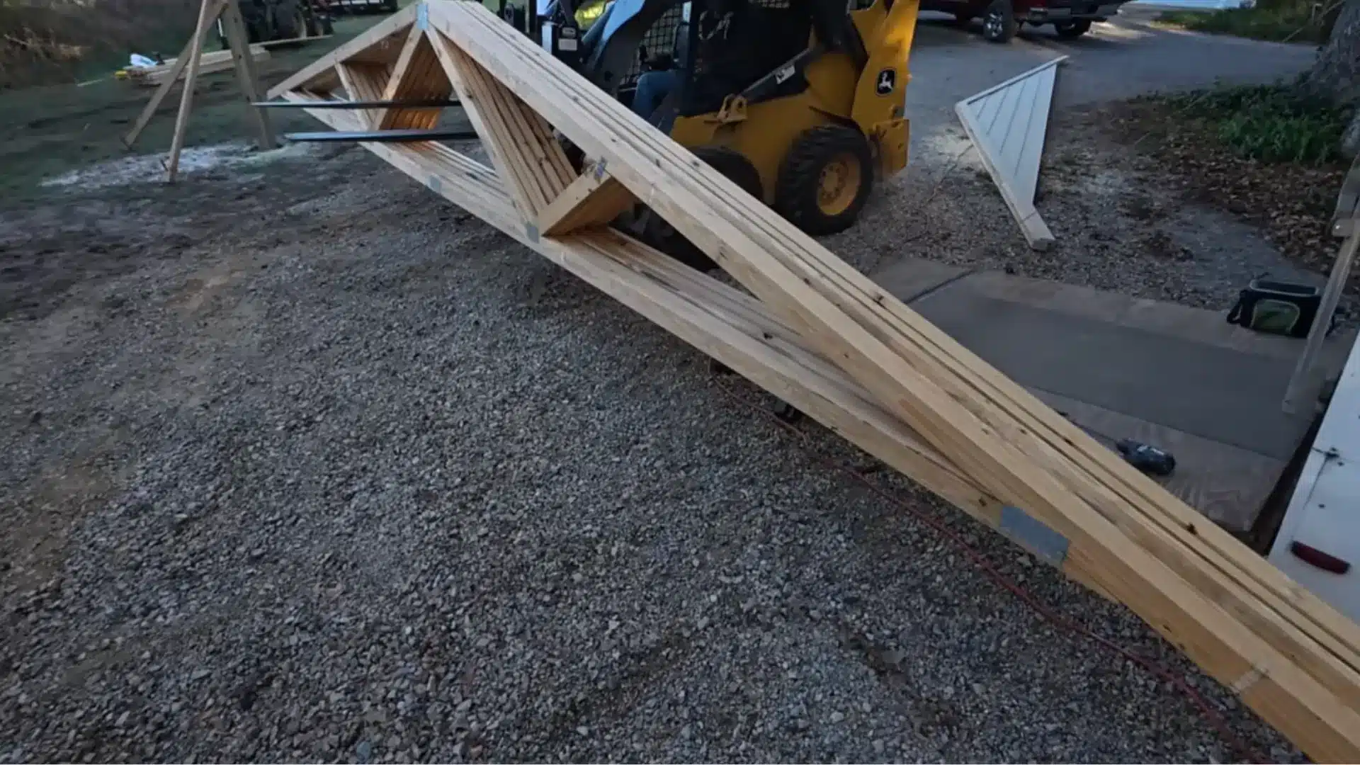 a yellow skid steer loader lifting a wooden beam into place at a carport building site