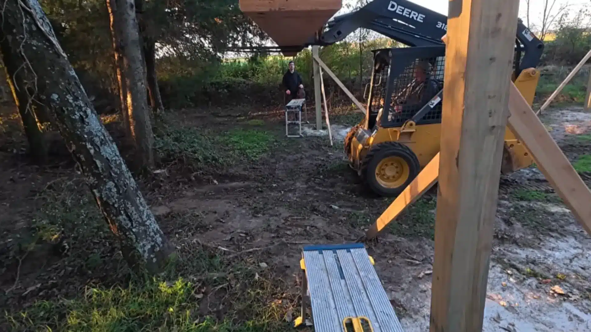 two men carefully positioning a large wooden roof truss along the top beam of a carport frame