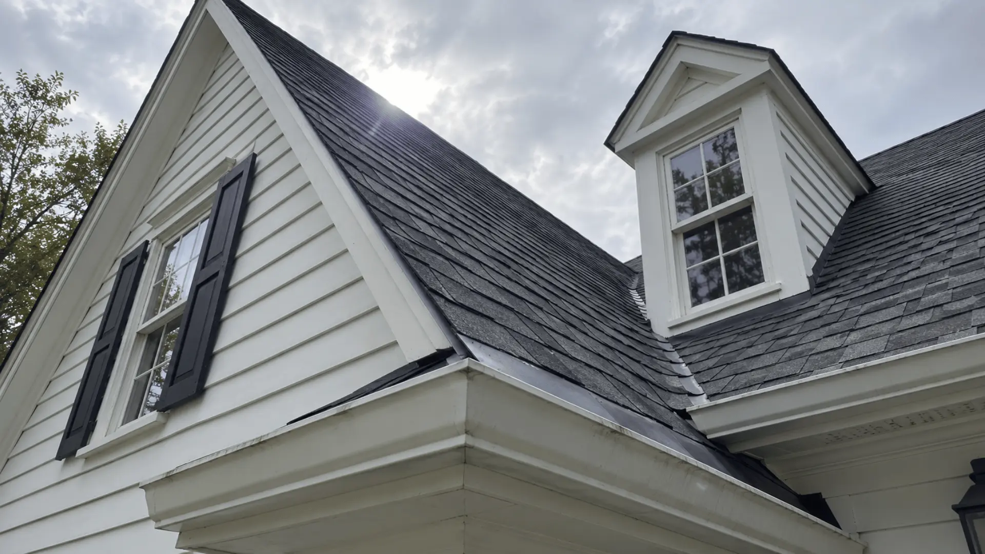 close-up of a colonial home's gabled roofline with shingles and a small dormer
