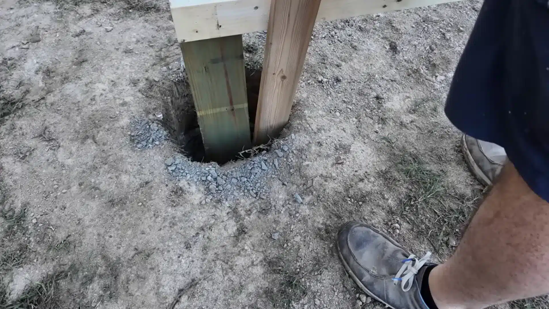 wooden support post set into a gravel filled hole ready for concrete during carport construction