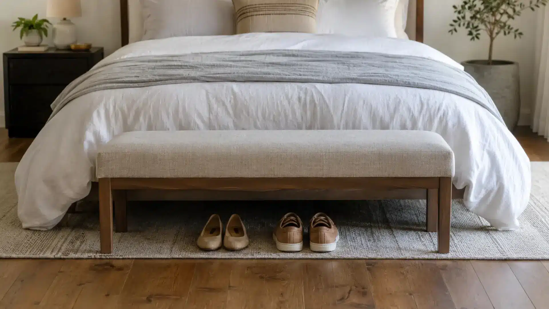 upholstered bench at the foot of a bed with shoes tucked neatly underneath on rug