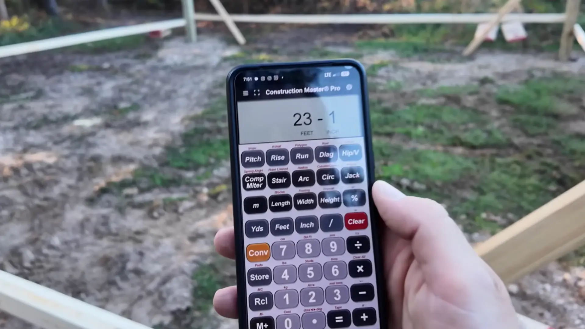 hand holding a construction calculator app displaying measurements at a carport building site