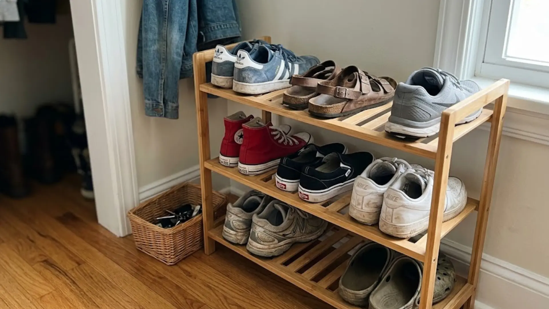 wooden tiered shoe rack holding sneakers sandals and casual shoes near entryway wall