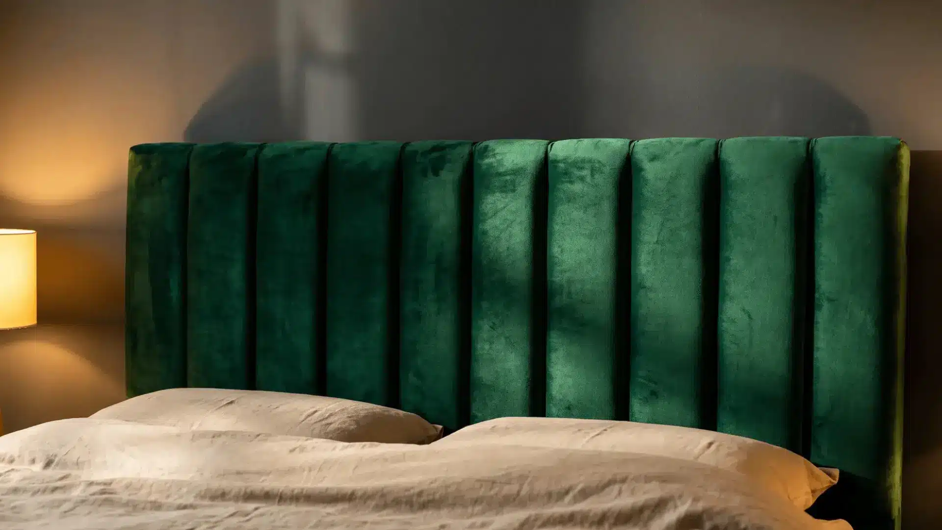 emerald green velvet headboard with cream bedding and warm bedside lighting in a bedroom