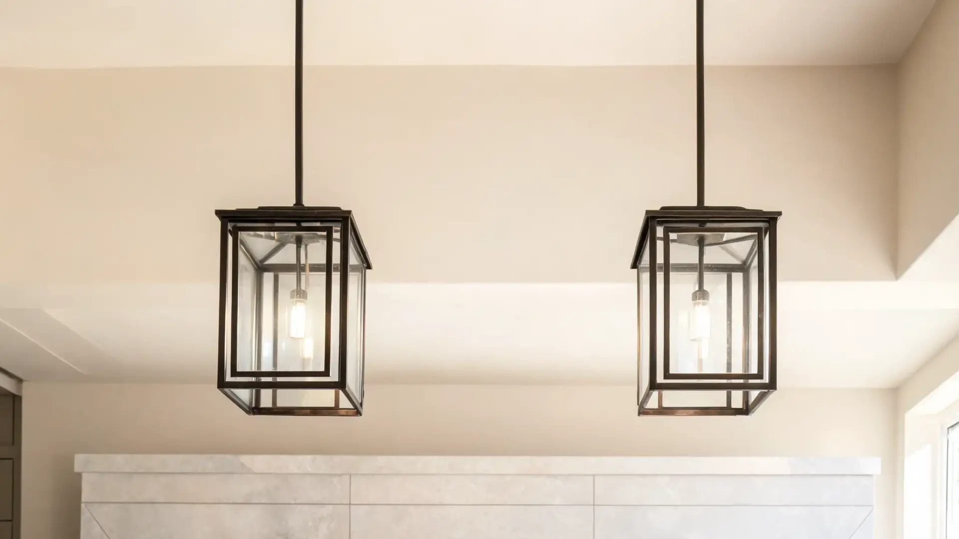 two black metal lantern pendant lights with glass panels hanging above a farmhouse kitchen island